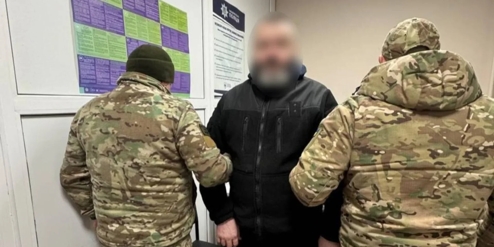 Двоє чоловіків у камуфляжі супроводжують чоловіка в чорній куртці з розмитим обличчям у коридорі