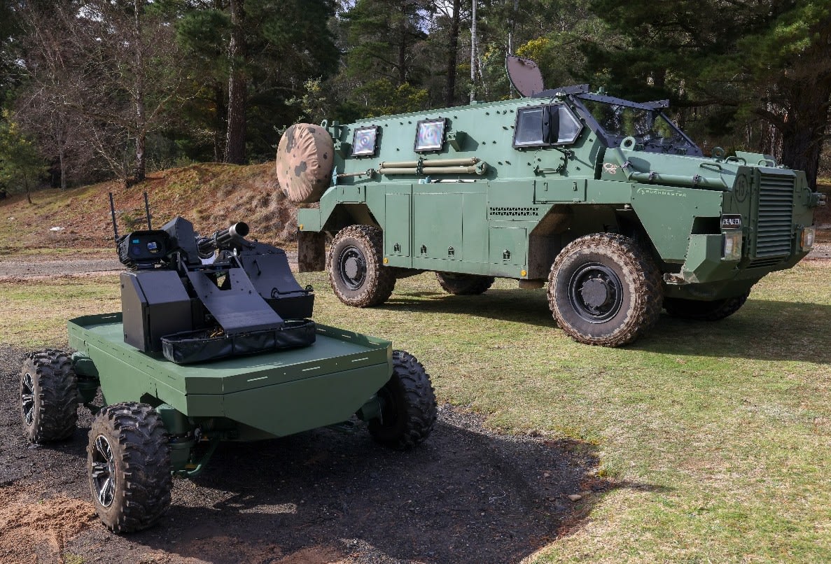 Озброєний зелений робот Guardian Angel поруч із бронетранспортером Bushmaster на полі біля лісу